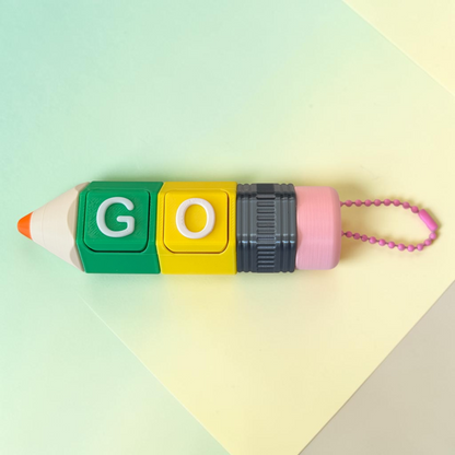 A pencil-shaped novelty fidget keychain  with colorful blocks spelling 'GO' in green and yellow, a dark gray ribbed middle section, and a pink eraser end with a pink bead chain, photographed on a pastel multicolor background.
