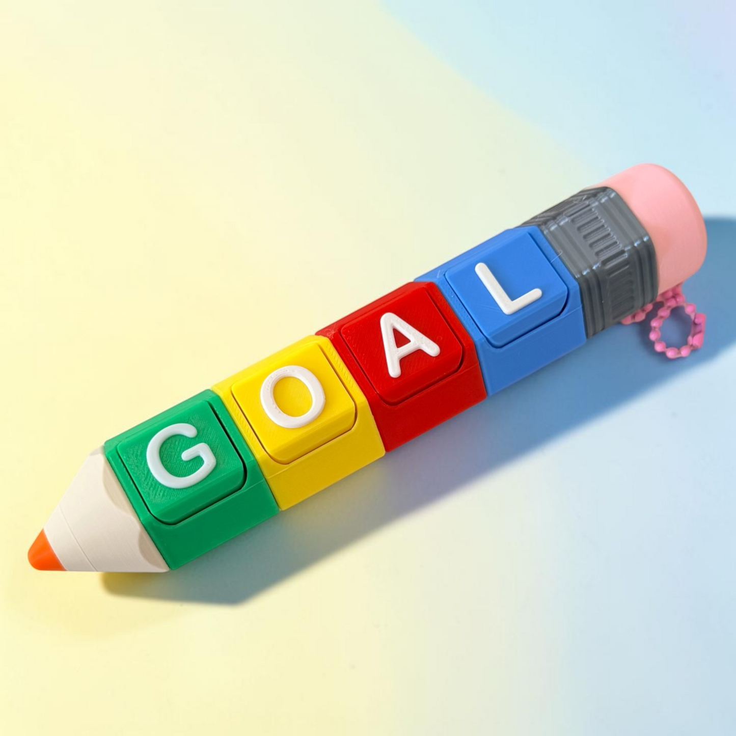 A novelty pencil-shaped fidget clicker on keychain  with colorful letter tiles spelling 'GOAL' in green, yellow, red, and blue, topped with a pink eraser and a small pink beaded loop.