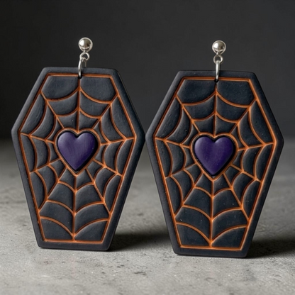 A pair of coffin-shaped earrings with a black and dark gray spiderweb pattern outlined in orange, featuring a purple heart in the center and silver-tone hooks.