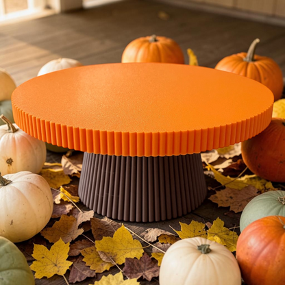 An orange and dark brown ribbed pedestal table surrounded by pumpkins and autumn leaves on a wooden floor.