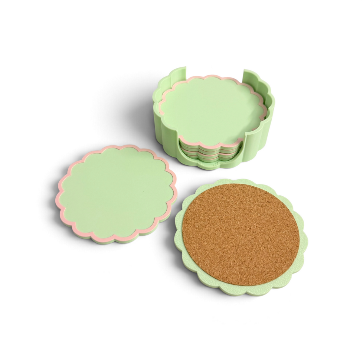 A set of scalloped circular coasters in pale green with pink edging, shown on a white background. One coaster is open to reveal a cork insert, and a stack of coasters is visible in the background.