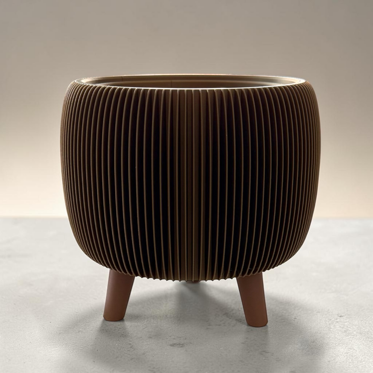 A modern cylindrical planter or decorative pot with a ribbed, pleated exterior and three short legs, shown on a neutral studio background.
