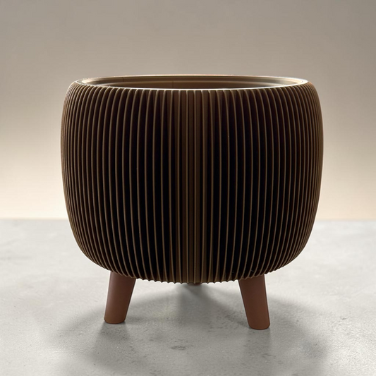 A modern cylindrical planter or decorative pot with a ribbed, pleated exterior and three short legs, shown on a neutral studio background.